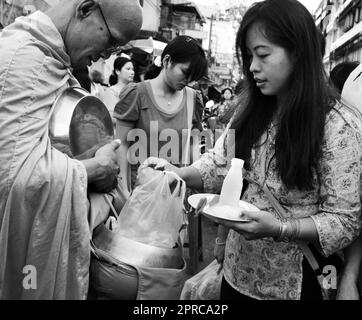 Ein thailändischer buddhistischer Mönch segnet die Einheimischen und empfängt Almosen im Rahmen eines morgendlichen Rituals. Foto in Bangkok, Thailand. Stockfoto