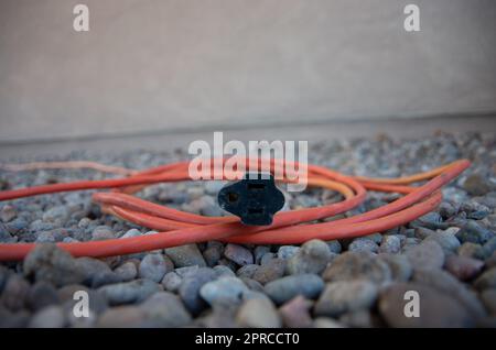 Orangefarbenes Verlängerungskabel für den Außenbereich im Felsenbett Stockfoto