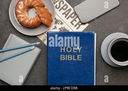 Heilige Bibel mit Notizbuch, Handy, Kuchen, Kaffeetasse und Zeitung auf dunklem Hintergrund Stockfoto