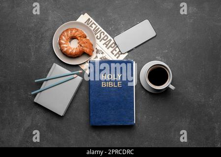 Heilige Bibel mit Notizbuch, Handy, Kuchen, Kaffeetasse und Zeitung auf dunklem Hintergrund Stockfoto