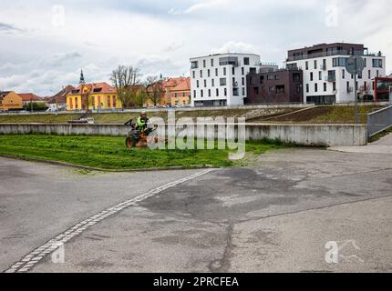 Ein Mann schneidet Gras am Ufer vor neuen Wohngebäuden Stockfoto