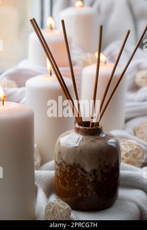 Aroma-Reed-Diffusor. Flaschenbehälter mit Holzstäbchen diffussiert ätherische Öle, um Ihr Heim Duft Konzept Herbsturlaub in gemütlichen Heim auf dem Fenstersill Hygge Ästhetische Atmosphäre auf gestricktem weißen Pullover. Stillleben im Mikromoment, aufrichtiges langsames Leben. Psychische Gesundheit Wohlbefinden Übungen regnen draußen Stockfoto