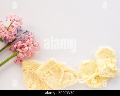 Rosafarbene und lila Hyazinthen-Blumen, gelbe Stiefel und Handschuhe für ein Neugeborenes auf weißem Hintergrund mit Kopierbereich. Muttertag Grußkarte. Schreib Weisheit Stockfoto