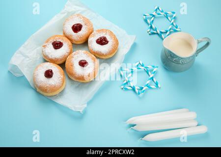 Hanukka süße Donuts Sufganiyot (traditionelle Donuts) mit Fruchtgelee und weißen Kerzen auf blauem Papierhintergrund. Jüdischer Urlaub Hanukkah Conc Stockfoto
