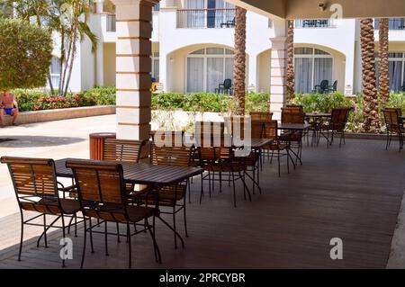 Ein offenes Café mit Holztischen und -Stühlen auf der Straße mit einer offenen Veranda in einem tropischen, warmen Land in einem Erholungsort mit Palmen. Stockfoto