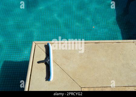 Eine blaue Bürste mit Schwamm zur Reinigung des Pools, die Fliesen auf dem Hintergrund des Pools mit flachen quadratischen Keramikfliesen und pflegt Stockfoto