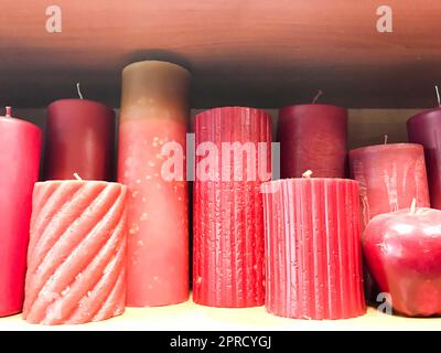 Die Konsistenz vieler festlicher verschiedener Formen von roten, burgunderroten Wachskerzen mit Dochten, die nacheinander stehen. Der Hintergrund. Stockfoto