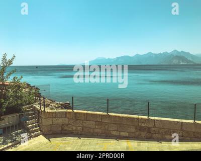 Meerblick vom kleinen Pier. Metallzaun auf Steinen. Zugang zum Meer vom Kieselstrand. Meer mit Blick auf einen großen Berg. Weg für Romantik w Stockfoto