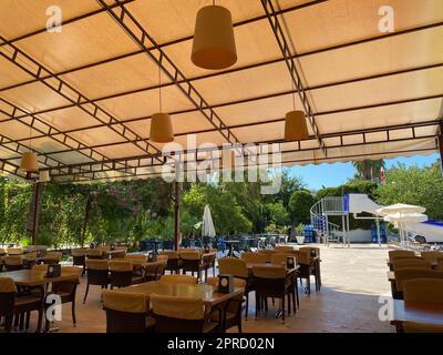 Ein offenes Cafe mit einem Bartisch mit Holztischen und -Stühlen auf der Straße mit einer offenen Veranda in einem tropischen warmen Land in einem Rest Resort mit Palmen tr Stockfoto