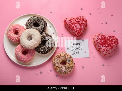 Donuts-Donuts mit Schokolade, Marshmallow und Zuckerstreuseln auf pinkfarbenem Hintergrund, Draufsicht. Farbenfrohe Karneval- oder Geburtstagskarte. Fröhliche Nationa Stockfoto
