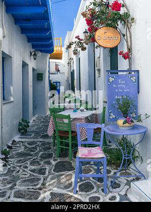 Ein typisch griechisches Restaurant in einer gepflasterten Straße mit weiß getünchten Gebäuden und hellen mediterranen Farben auf der Insel Milos, Griechenland Stockfoto