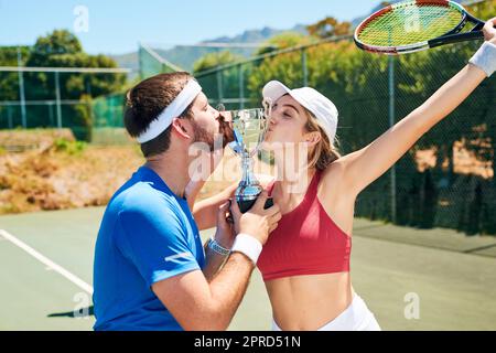 Wir trainierten hart für diese Trophäe. Zwei junge Sportler standen zusammen und küssten eine Trophäe, nachdem sie ein Tennismatch gewonnen hatten. Stockfoto