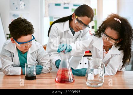 Ihre erste Einführung in die Chemie war eine lustige. Ein süßer kleiner Junge und ein süßes Mädchen, die ein wissenschaftliches Experiment mit ihrem Lehrer in der Schule durchführen. Stockfoto