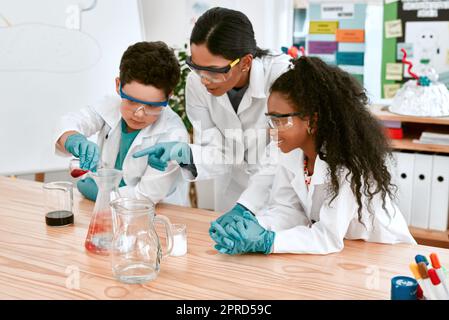 Der Science-Kurs macht so viel Spaß. Ein entzückendes kleines Mädchen und ein Junge führen ein wissenschaftliches Experiment mit ihrem Lehrer in der Schule durch. Stockfoto