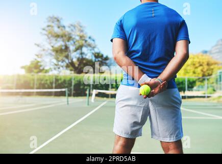 Got Game Lets Play. Rückansicht eines nicht erkennbaren männlichen Tennisspielers, der einen Tennisball auf einem Platz im Freien hält. Stockfoto