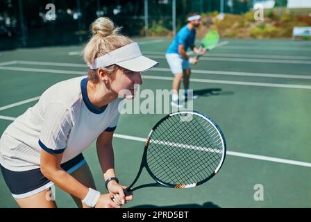 Die Gewinner verlieren nie ihren Fokus. Eine attraktive junge Tennisspielerin spielt zusammen mit einem männlichen Teamkollegen im Freien auf einem Platz. Stockfoto