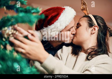 Kein Mistel, kein Problem. Ein liebevolles junges Paar schmückt ihren Weihnachtsbaum zu Hause zusammen. Stockfoto