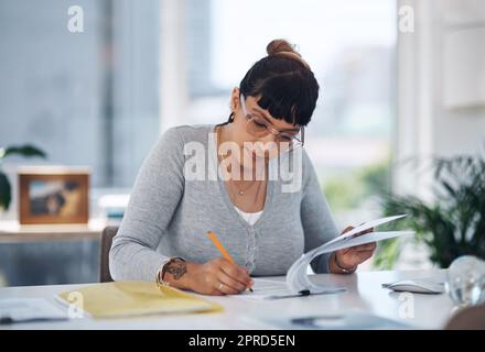 Ich muss diese Information ändern: Eine attraktive junge Geschäftsfrau, die allein in ihrem Büro sitzt und Papierkram durchliest. Stockfoto