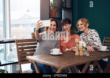 Eine Gruppe von attraktiven Frauen mittleren Alters, die zusammen ein Selbstporträt machen, während sie tagsüber in einem Café sitzen. Stockfoto