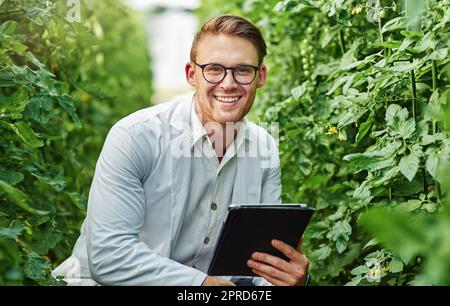 Ich liebe es einfach, draußen zu forschen. Porträt eines gutaussehenden jungen Wissenschaftlers, der ein digitales Tablet benutzt, während er Pflanzen und Kulturen im Freien auf einem Bauernhof studiert. Stockfoto
