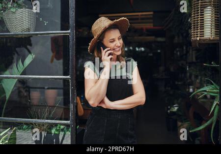 Ich mache auch Call-in-Lieferungen. Eine attraktive junge Geschäftsbesitzerin, die allein am Eingang ihrer Floristik steht, während sie an einem Telefongespräch telefoniere. Stockfoto