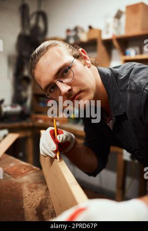 Ich bin sehr beschäftigt. Porträt eines fokussierten jungen Zimmermanns, der nachts auf einem Holzstück in einer Werkstatt Messungen durchführt. Stockfoto