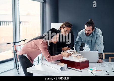 Dieses Projekt braucht unsere ganze Expertise. Drei junge Architekten arbeiten in ihrem Büro an einem maßstabsgegliedrigen Modell eines modernen Hauses. Stockfoto