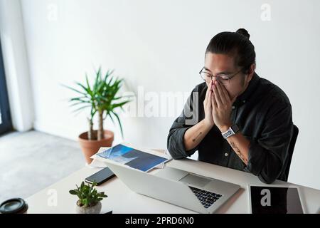 Mein Stresslevel ist auf einem Allzeithoch. Ein hübscher junger Geschäftsmann, der gestresst aussieht und bei der Arbeit unter Kopfschmerzen leidet. Stockfoto