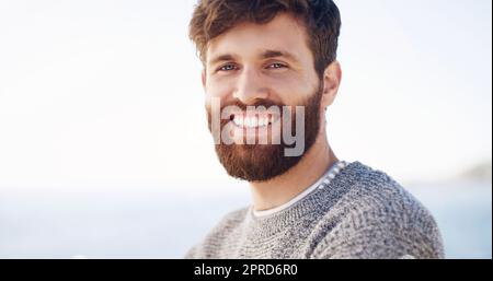 Lächeln Sie weiter, wachsen Sie den Bart. Ein hübscher junger Mann, der den Tag am Strand verbringt. Stockfoto