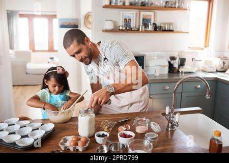 Vergessen Sie nicht die Zutaten, die es süß macht. Ein junger Mann, der zu Hause mit seiner jungen Tochter backt. Stockfoto