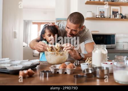 Du musst dich schmutzig machen, um Spaß zu haben. Ein junger Mann, der mit seiner kleinen Tochter zu Hause backt. Stockfoto