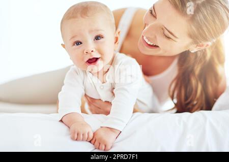 Mutter und süßer, neugeborener Junge, die sich als Familie im Schlafzimmer zu Hause zusammentun. Glückliche, lächelnde und sorgenfreie mutter und Sohn, die Liebe und Zuneigung zeigen, während sie sich morgens auf einem Bett entspannen Stockfoto