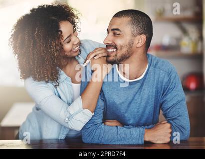 Liebevolles, fürsorgliches und lächelndes Paar in einer Küche zu Hause. Mann und Frau sehen sich an, in Liebe, Freude und Glück. Junge Romantiker, die drinnen einen liebevollen Moment miteinander verbringen Stockfoto