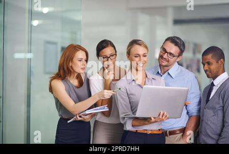 Manager mit Laptop, der Strategievorschläge zeigt, schult oder präsentiert oder Brainstorming-Pläne mit verschiedenen Kollegen aus dem Büro durchführt. Selbstbewusste, lächelnde oder glückliche Führungskraft, die das Team über Technologie informiert Stockfoto