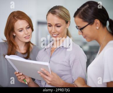 Teamleiter zeigt Strategievorschläge auf Papier und trifft kreative Kollegen im Büro. Junge, motivierte und interessierte Gruppe von Geschäftsfrauen, die zusammenstehen und beim Brainstorming Papierkram verwenden Stockfoto