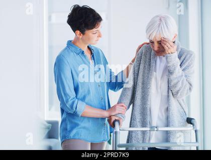 Mein Kopf ist ein wenig wund. Eine liebevolle junge Frau hilft ihrer älteren Mutter, die zu Hause unter Kopfschmerzen leidet. Stockfoto