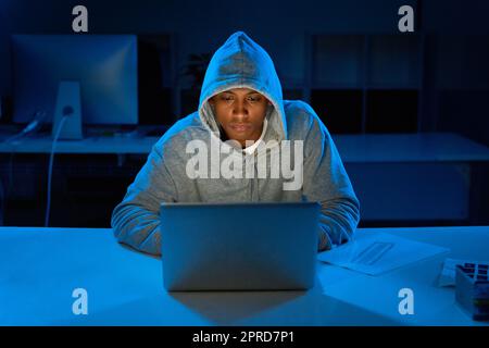 Hacking in den späten Stunden der Nacht. Ein junger männlicher Hacker mit einem Laptop im Dunkeln. Stockfoto