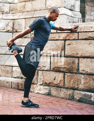 Die Vorbereitung ist immer der Schlüssel. Ganzkörperaufnahme eines hübschen jungen Sportlers, der sich vor dem Training im Freien in der Stadt dehnt und wärmt. Stockfoto