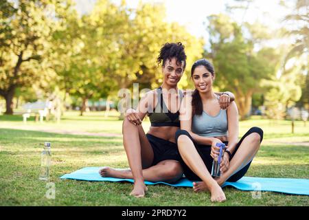 Gemeinsam können wir alles erreichen. In voller Länge Porträt von zwei attraktiven jungen Frauen, die dicht beieinander sitzen und lächeln, während sie im Park sind. Stockfoto