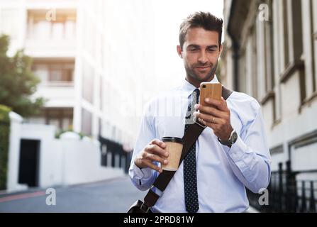 Am frühen Morgen telefoniert ein hübscher junger Geschäftsmann, der auf seinem Handy SMS schreibt, während er morgens zur Arbeit geht. Stockfoto