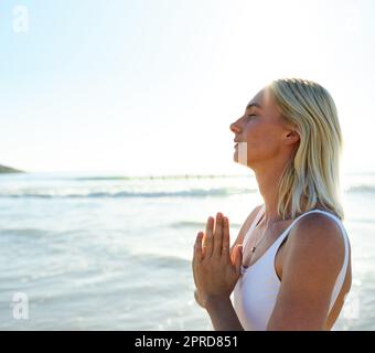 Die Ruhe in meiner Seele finden. Eine attraktive junge Frau, die am frühen Morgen am Strand meditiert. Stockfoto