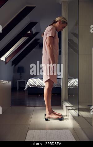 Shes nahe an der Erreichung ihrer Fitnessziele. Ganzkörperaufnahme einer jungen Frau, die sich zu Hause auf einer Waage wägt. Stockfoto