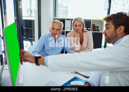 Meine Testergebnisse zeigen, dass es sich hier um den infizierten Bereich handelt. Ein Arzt bespricht die Befunde am Computer mit einem älteren Mann und seiner Tochter in der Klinik. Stockfoto