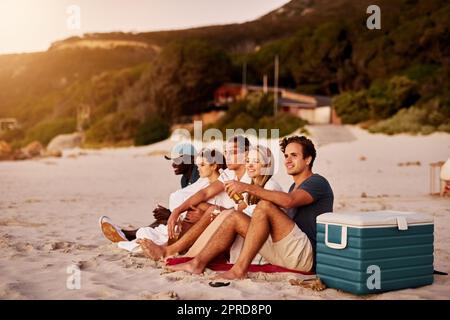 Genießen Sie schöne Landschaft mit schönen Menschen. Eine Gruppe von Freunden sitzen zusammen am Strand. Stockfoto