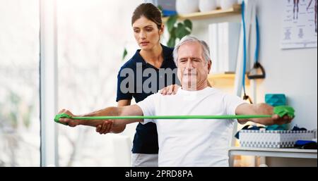 HES arbeitet hart, um aktiv und gesund zu bleiben. Eine attraktive junge Physiotherapeutin, die mit einem älteren männlichen Patienten zusammenarbeitet. Stockfoto