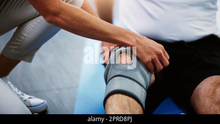 Vorsichtige Maßnahmen bis zur vollen Fitness. Eine unkenntliche Physiotherapeutin schnürt einen männlichen Patienten mit einer Kniebandage. Stockfoto