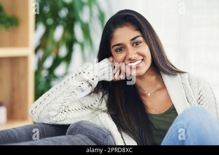 Ihr Körper braucht diese Entspannung ab und zu. Beschnittenes Porträt einer glücklichen jungen Frau, die sich zu Hause auf der Couch entspannt. Stockfoto