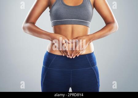 Liebe deinen Körper, indem du dich um ihn kümmere. Beschnittene Studioaufnahme einer nicht erkennbaren jungen Frau, die sich eine Herzform auf ihrem Bauch anmacht. Stockfoto