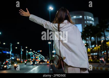 Eine Geschäftsfrau, die in der belebten Straße nachts mit einem Hageltaxi winkt, winkt Stockfoto