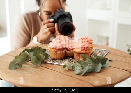 Eine attraktive junge Geschäftsfrau, die mit ihrer Kamera Cupcakes für ihren Blog fotografiert. Stockfoto